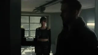 man and woman standing in dimly lit room — Blade Runner 2049