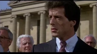 man in suit speaking by building columns — Rocky III