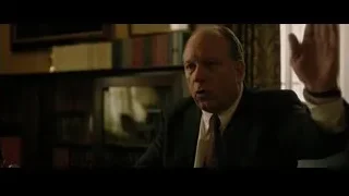 Man in suit gesturing in room with bookshelf — The Social Network